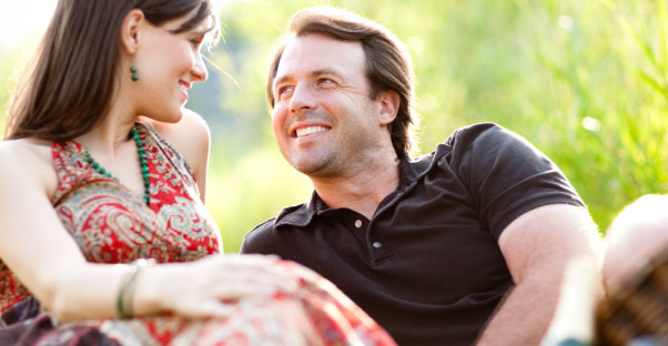 A couple reclines in a scenic tall grass scene and gaze into each other's eyes.