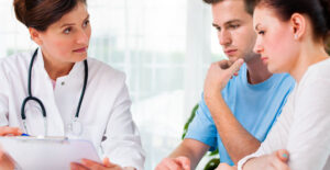 A young couple and a doctor examine a patient chart.