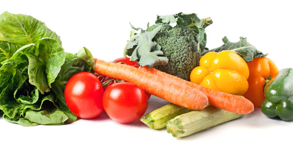 A pile of vegetables, including carrots, tomatoes, zucchini, and yellow bell peppers.