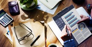 Image of a cluttered desk with graphs and charts and glasses