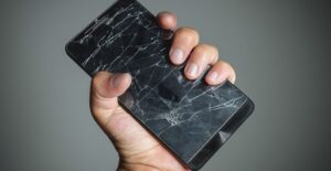 Hand clutching a phone with a shattered screen