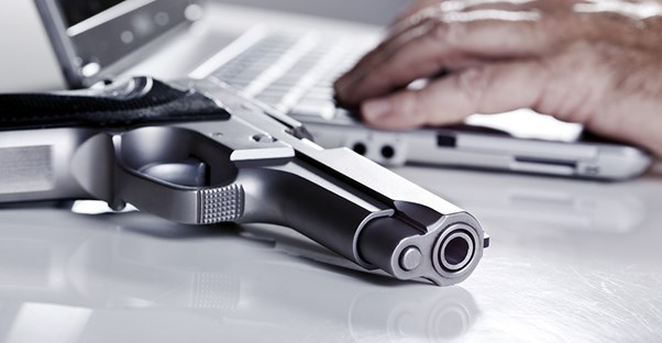 Man on laptop computer with gun next to him