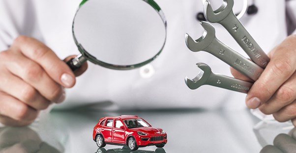 Car doctor examining a miniature broken car with tools
