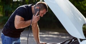 Man leaning over the open hood of a broken down car