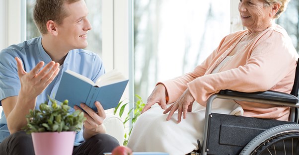 man reading to senior in wheelchair