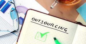 outsourcing written on notepad with coffee and glasses and charts
