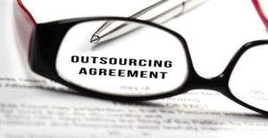 glasses and pen on top of outsourcing agreement contract