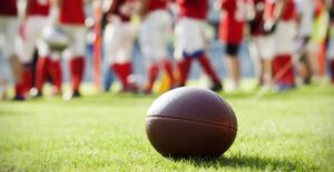 Football laying on field with players in the background