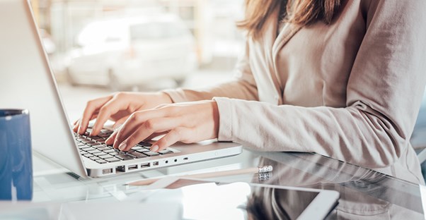 woman typing on laptop computer with tablet sitting nearby
