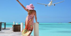 A woman on a pier waves goodbye to a departing plane.