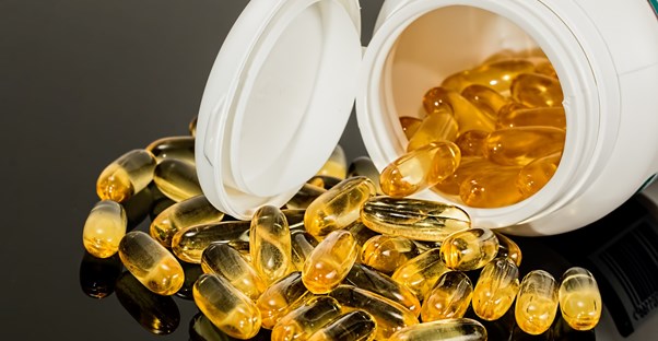 A bottle of medication has yellow translucent capsules spilling out of it.