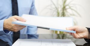 two men at desk exchanging stack of employment papers