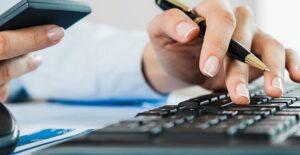 Woman with phone in one hand and pen in the other resting on keyboard researching asset management software