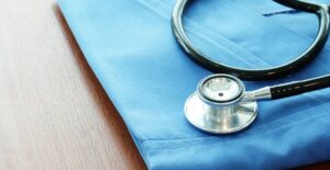 black and silver stethoscope resting on top of neatly folded blue scrubs laying on a brown wooden table.