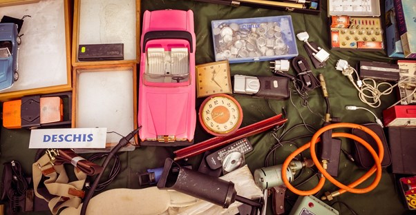 Antique items and old parts cover a table at a yard sale.
