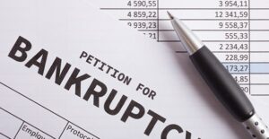 ink pen resting on a sheet of paper that is a petition for bankruptcy with a number chart peeking out from behind it to show pros and cons