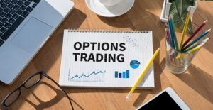 Notebook with notes on options trading statistics sitting on desk with glasses, open laptop, pencils in a cup, a latte, and a small plant