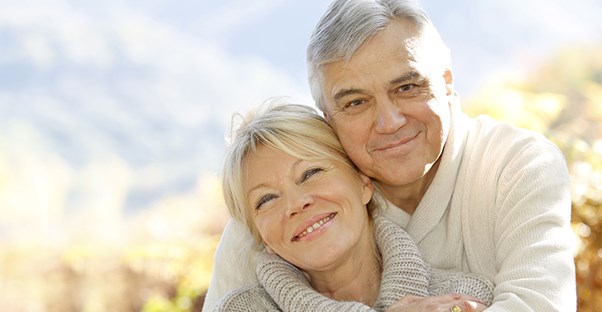 Senior couple posing happily in front of a beautiful mountain background smiling because they found a great insurance policy