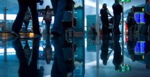 Passengers walk through a busy airport concourse toward airport security.