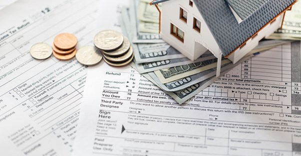 A toy house sitting on top of cash mortgage tax deduction on top of tax filing forms on a desk