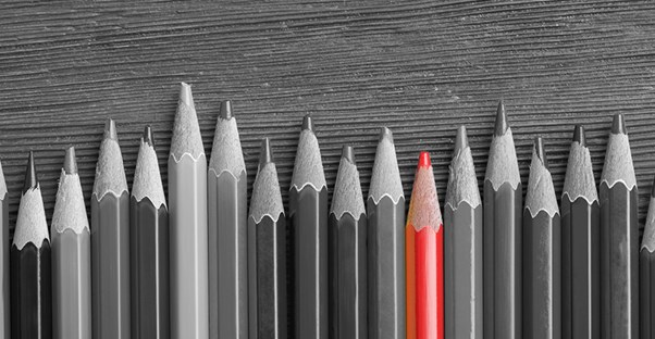 black and white photo of pencils lined up on a special education teacher's desk, with one pencil colored in red.