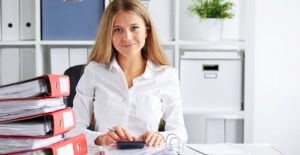 Woman at desk with binders and a calculator. Actuary vs accountant.