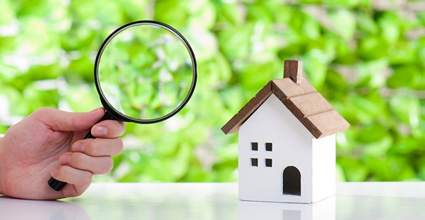 Magnifying glass looking at a toy house. Home inspections.