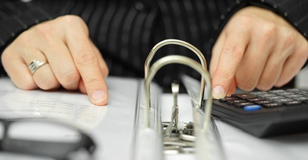 Person checking a binder and calculator. Payroll and 401K.