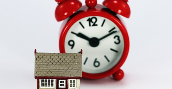 Small house sitting next to an alarm clock to represent good timing for home refinancing