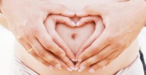 Pregnant belly with hands in a heart. Pregnancy and constipation.
