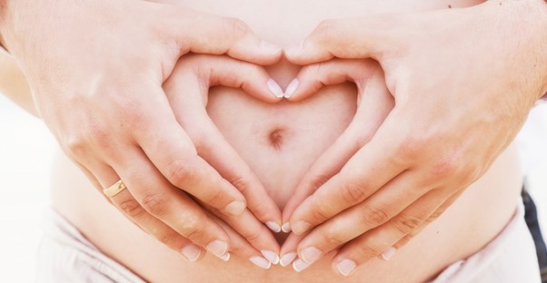 Pregnant belly with hands in a heart. Pregnancy and constipation.