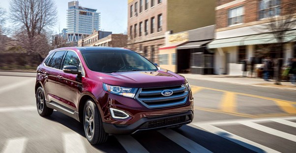 a maroon 2018 ford edge drives down a city street