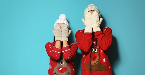a young couple wearing ugly christmas sweaters on blue background