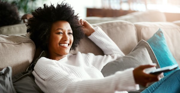 a woman on her couch using her remote control to enjoy HBO on her television