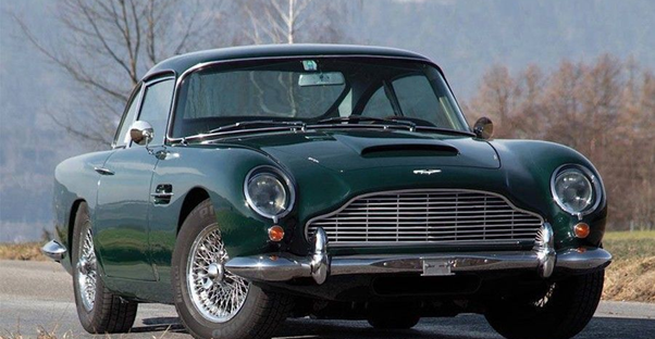 A dark green Aston Martin DB5 driving down a road