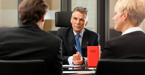 Serious looking professional man sitting across a desk from a pair of people