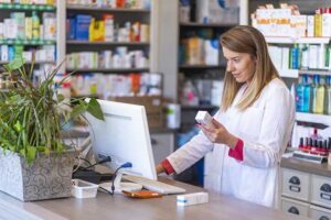 A pharmacist examines medication and checks a computer in the pharmacy.