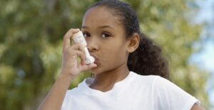 a young girl stops playing to use her inhaler for her asthma