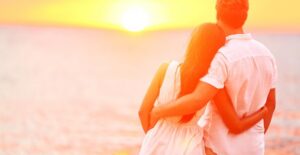 a honeymooning couple embraces in front of an ocean sunset