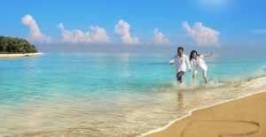 a couple holding hands running along the ocean with a heart drawn in the beach sand