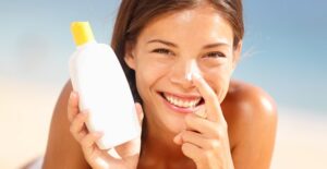Woman applies sunscreen to her nose on the beach