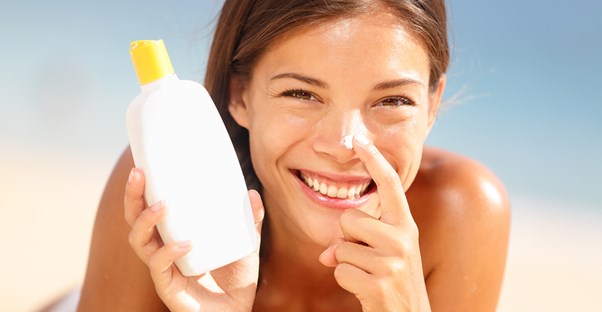 Woman applies sunscreen to her nose on the beach