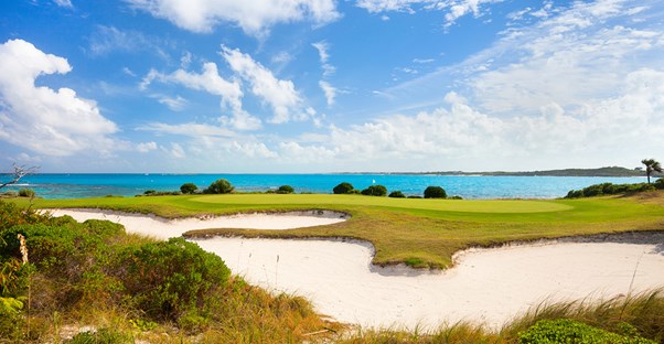 a sand bunker next to a golf green with the ocean in the background