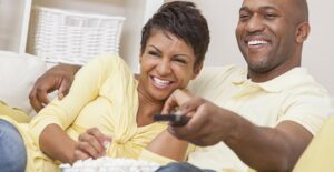 a couple sits down with popcorn to watch a movie at home
