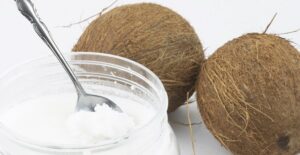 A jar of coconut oil next to two small coconuts