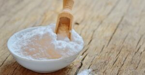 Bowl of baking soda with a wooden scoop standing in it.