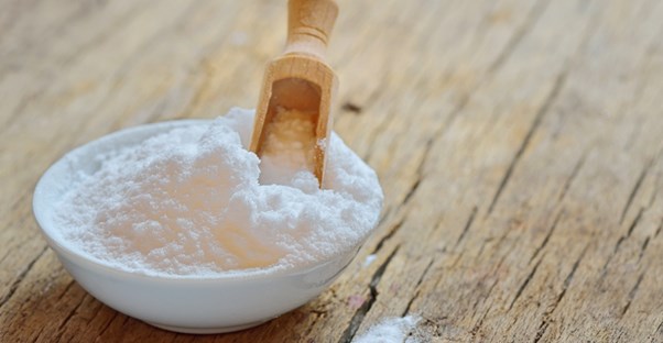 Bowl of baking soda with a wooden scoop standing in it.