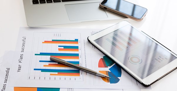 A computer, pen, tablet, cell phone, and charts tracking index funds.