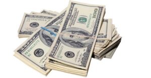 A stack of rubber-banded one hundred dollar bills gain from taking out a guarantor loan.
