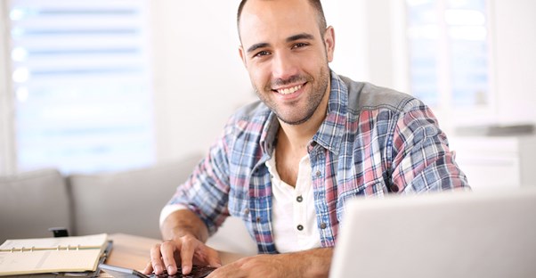 Man smiling as he checks on his online savings account from his computer at home.